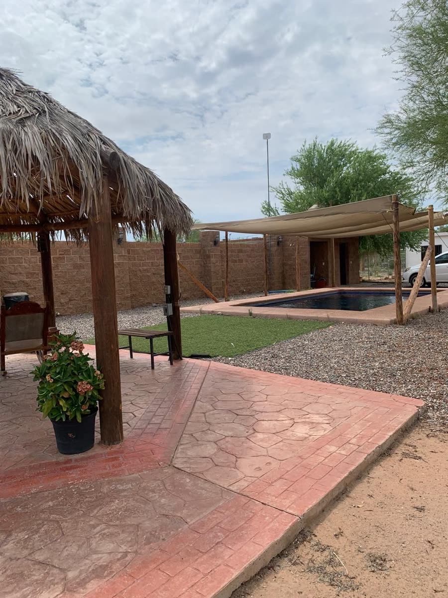 Patio con piso de piedra y palapa, con muro de adobe al fondo