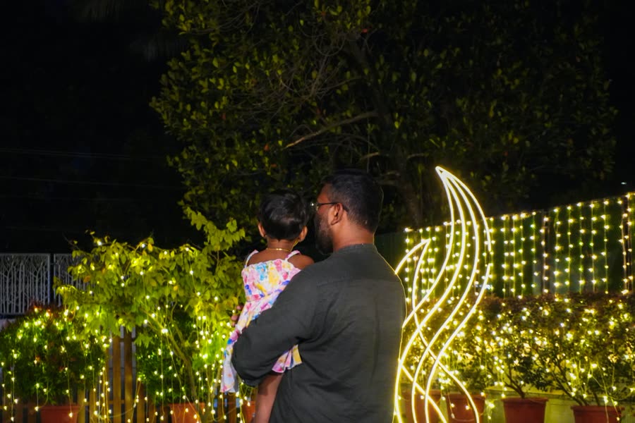 Un papá cargando a su hija frente a un jardín cubierto de luces de cadena
